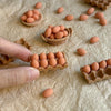 A hand is holding a small wooden tray filled with brown eggs on a wrinkled paper surface.