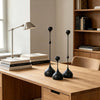 A set of three matte black waterdrop design candle holders displayed on a wooden table next to a desk lamp.