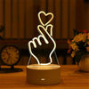 A glowing acrylic hand gesture heart night light resting on a wooden table.