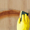 A hand in a yellow glove is peeling off a section of wood grain wall tiles from a wooden surface.