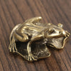 Antique brass frog sculpture decor resting on a dark wooden surface.
