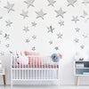 A white crib decorated with pink and gray stars, set against a white wall backdrop.