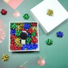 A collection of holographic star gift bows in various colors, including red, green, blue, and gold, displayed on a light gree