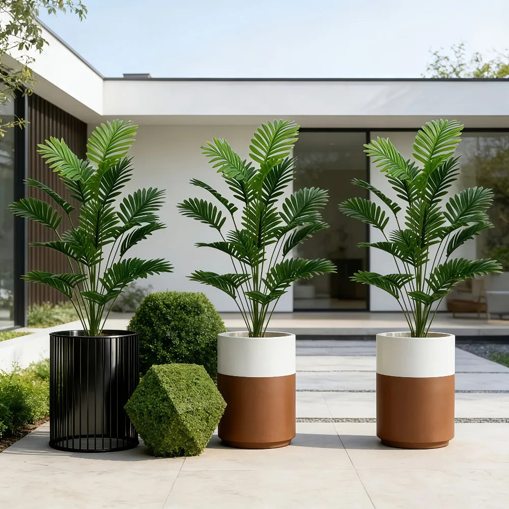 Three potted artificial palm trees with green leaves displayed on a light-colored patio surface.