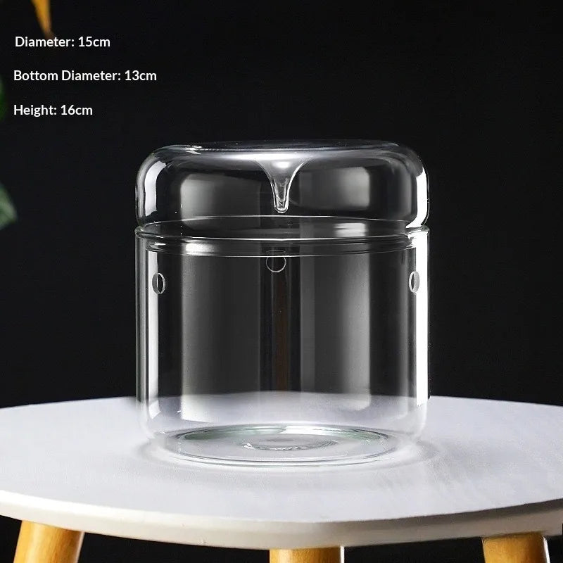 A clear glass decor vase with a wide mouth and a narrower bottom, sitting on a white surface.