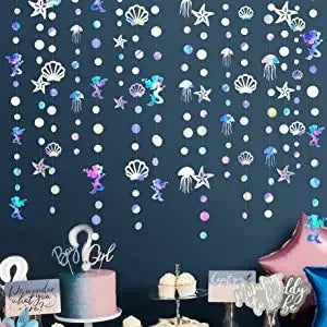 Iridescent mermaid and jellyfish party streamers hanging against a dark blue wall.