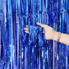 A hand is pulling down blue metallic foil fringe curtain streamers.