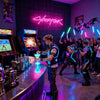 A person stands in front of a neon sign that reads Cyberpunk, surrounded by gaming equipment and colorful lighting.