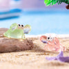 A set of luminous resin mini crab decor, featuring a green and pink crab, resting on light sand.