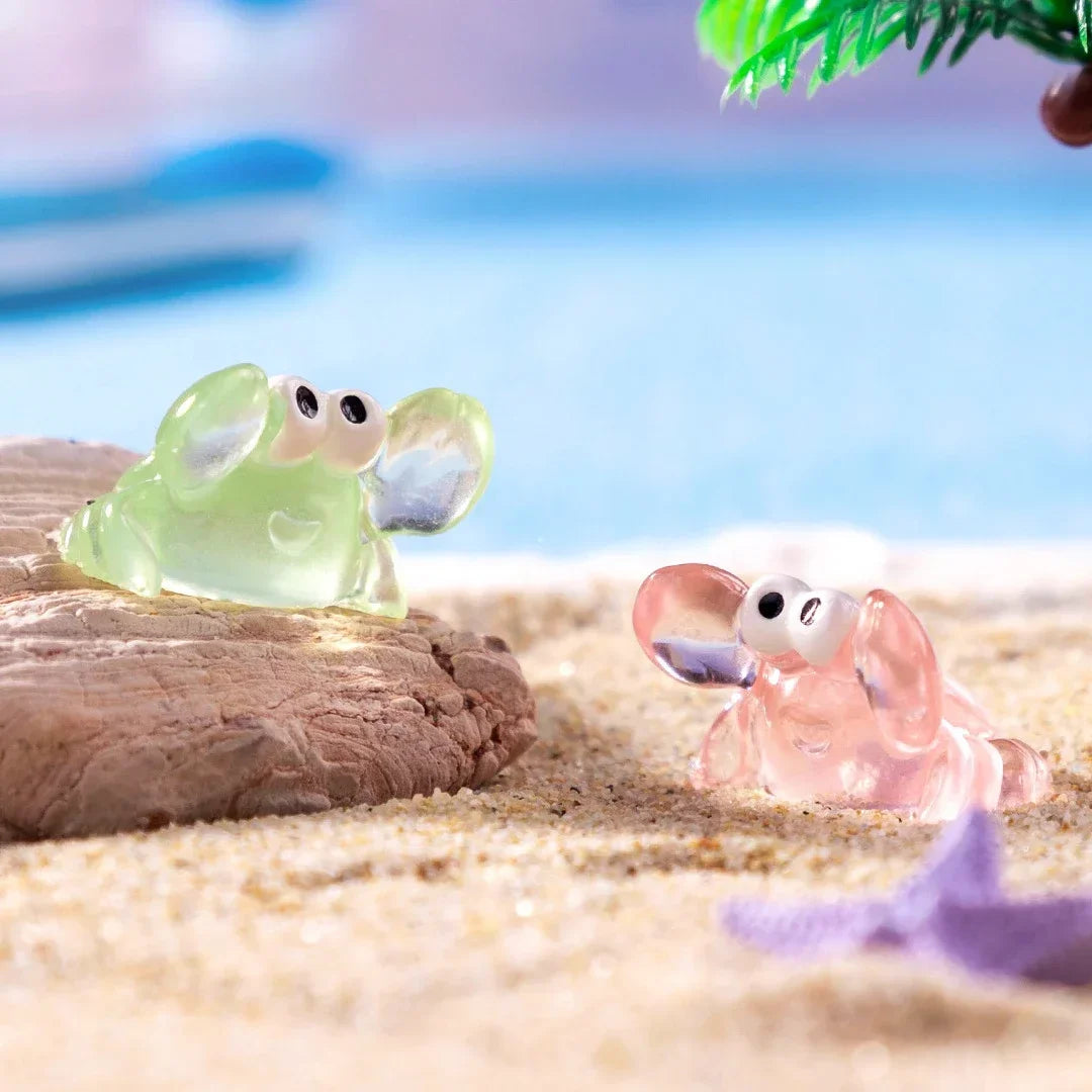 A set of luminous resin mini crab decor, featuring a green and pink crab, resting on light sand.