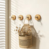 A woven natural fiber basket with dried flowers hangs on a light wood wall hook rack.