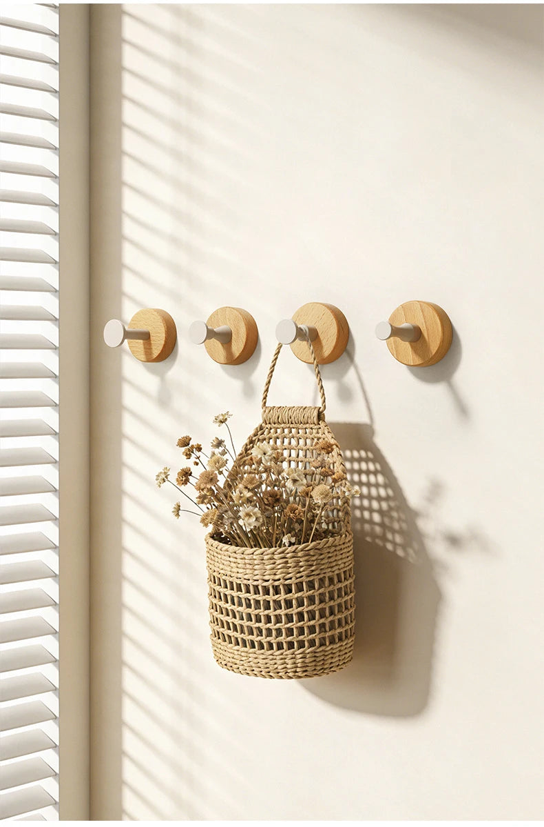 A woven natural fiber basket with dried flowers hangs on a light wood wall hook rack.