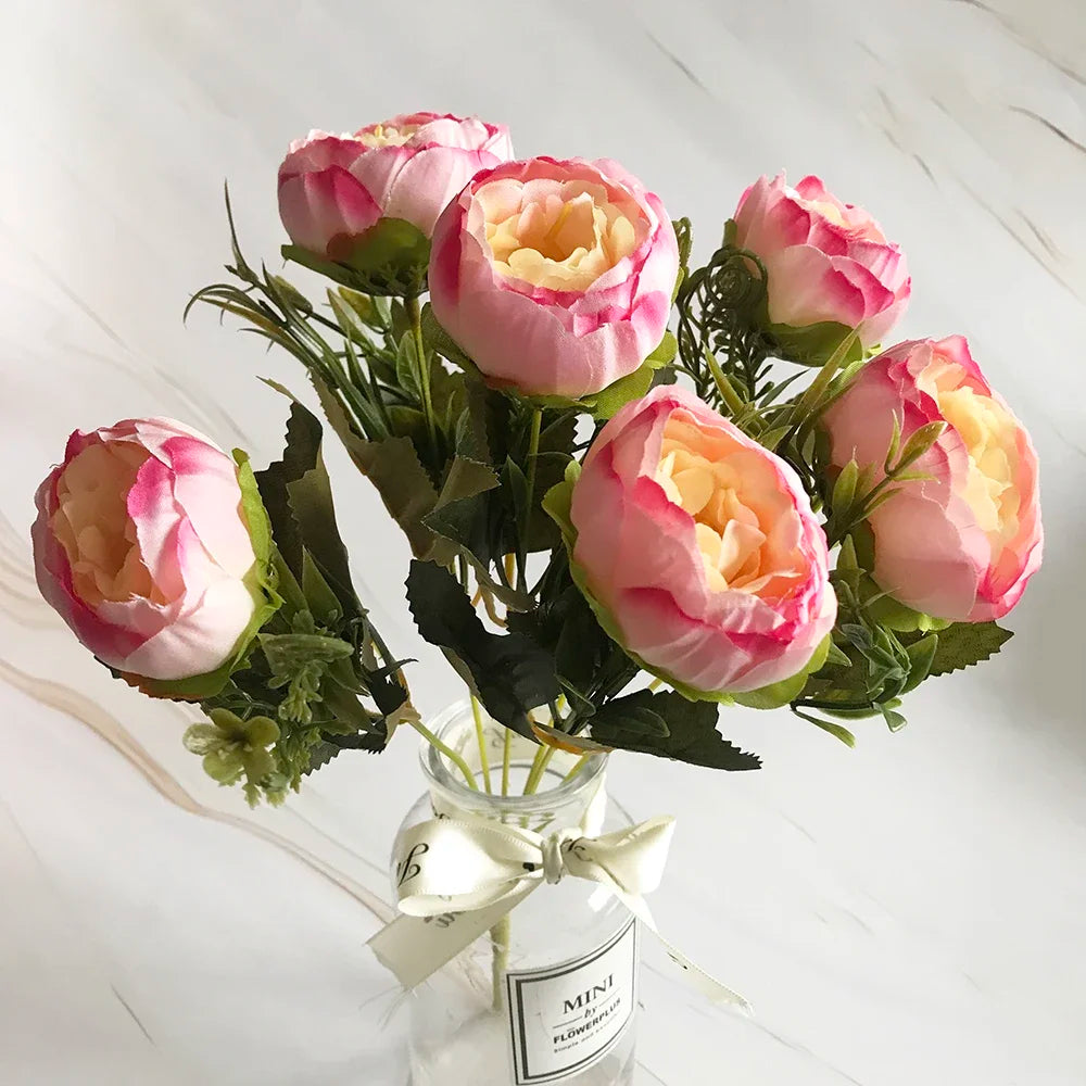 A bouquet of pink and peach silk rose and peony artificial flowers displayed in a glass jar.