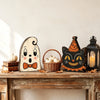A set of retro wooden block Halloween decor featuring a carved cat face, pumpkins, and autumn leaves on a rustic wooden surfa