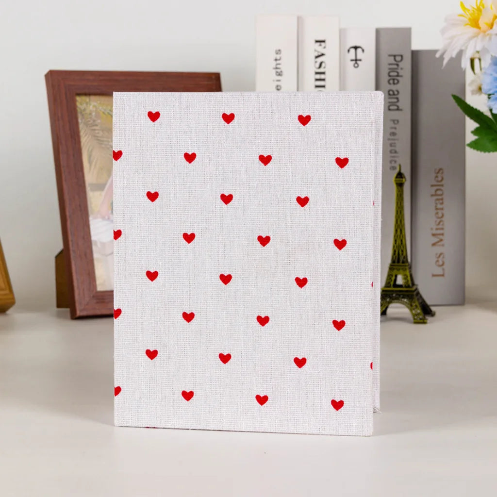 A white photo album cover with a red heart pattern, displayed next to books and a miniature Eiffel Tower.