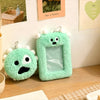 A pair of green fuzzy plush keychains with clear photo holders displayed on a wooden surface.