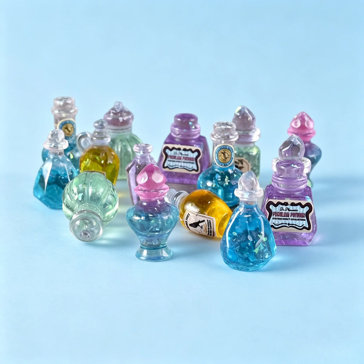 A collection of miniature resin magic potion bottles in various shades of purple, blue, and yellow arranged on a light blue s