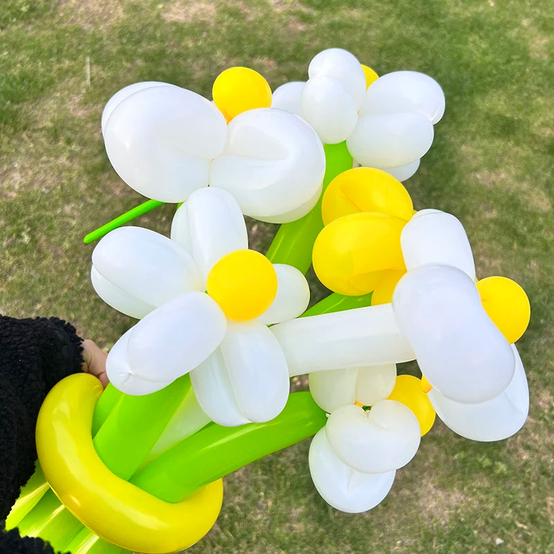 A cluster of white and yellow twisting balloons arranged in a decorative shape on green stems.