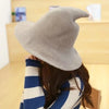 A beige knit witch hat worn by a person, featuring a pointed crown and wide brim.