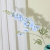 Un brin de fleurs artificielles de delphinium bleu clair sur un fond de rideau blanc.
