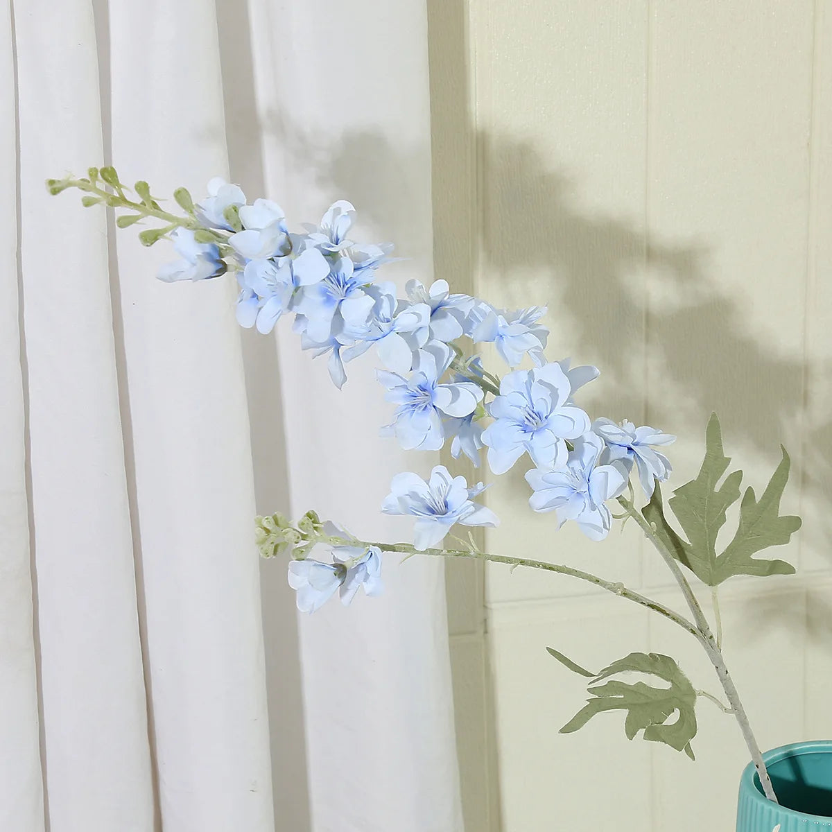 Un brin de fleurs artificielles de delphinium bleu clair sur un fond de rideau blanc.