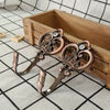 A pair of vintage rose gold crown curtain hooks with sparkling stones resting in a wooden box.