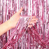 A hand is holding and displaying metallic pink foil fringe curtain streamers.