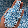 A hand holds a cluster of light blue pastel foam beads for crafting and decoration.