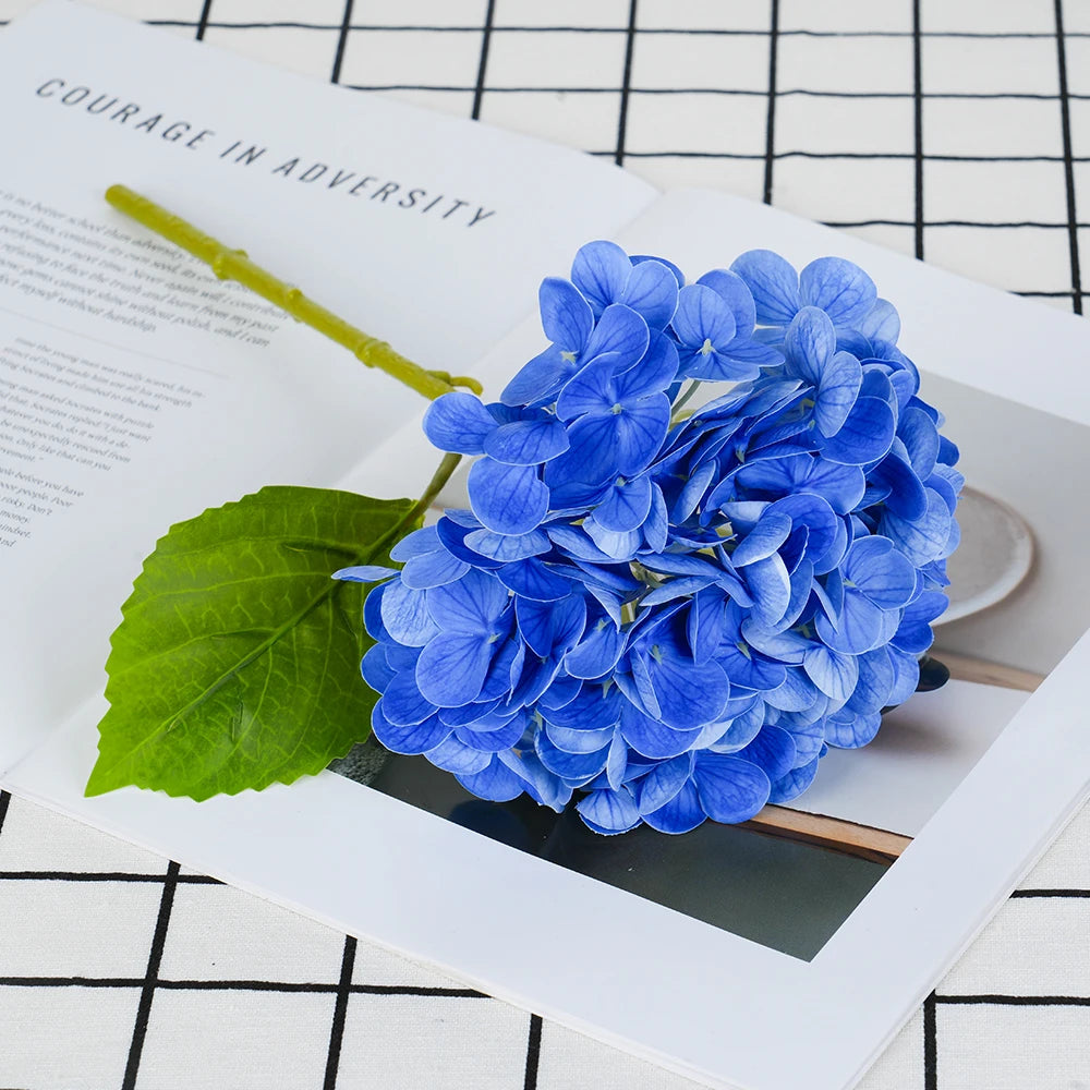 A vibrant blue artificial hydrangea flower is displayed on a white card next to text about courage.