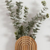 A lush green eucalyptus garland draped over a round wooden planter on a white wall.