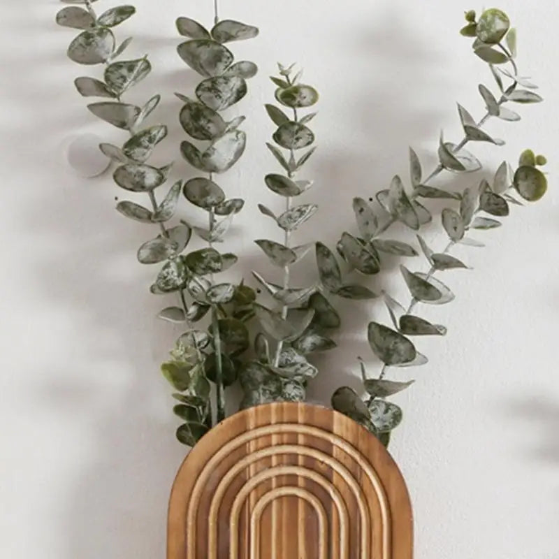 A lush green eucalyptus garland draped over a round wooden planter on a white wall.