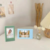 A small blue film frame displaying two women smiling, placed on a white table next to other framed photos.