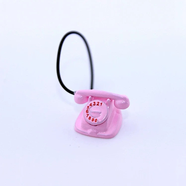 A pink vintage rotary desk phone miniature with a black cord against a white background.