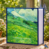 A blue laminated photo album featuring a watercolor landscape of green rolling hills and clouds.