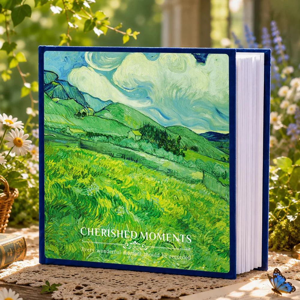A blue laminated photo album featuring a watercolor landscape of green rolling hills and clouds.