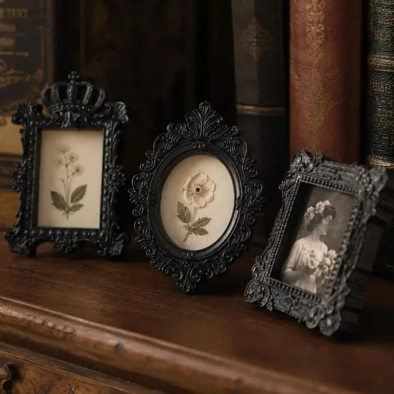 Three vintage resin mini picture frames displayed on a wooden surface next to old books.