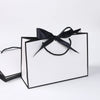 A set of five elegant black and white gift bags tied with black ribbon bows.