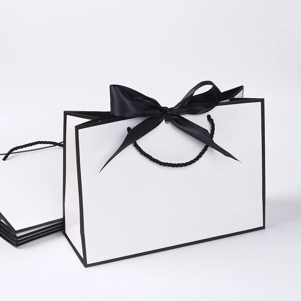 A set of five elegant black and white gift bags tied with black ribbon bows.