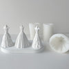 White silicone molds shaped like wedding dresses displayed next to white candles.