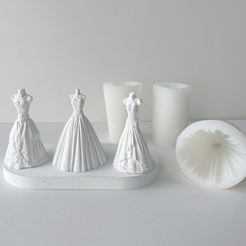 White silicone molds shaped like wedding dresses displayed next to white candles.