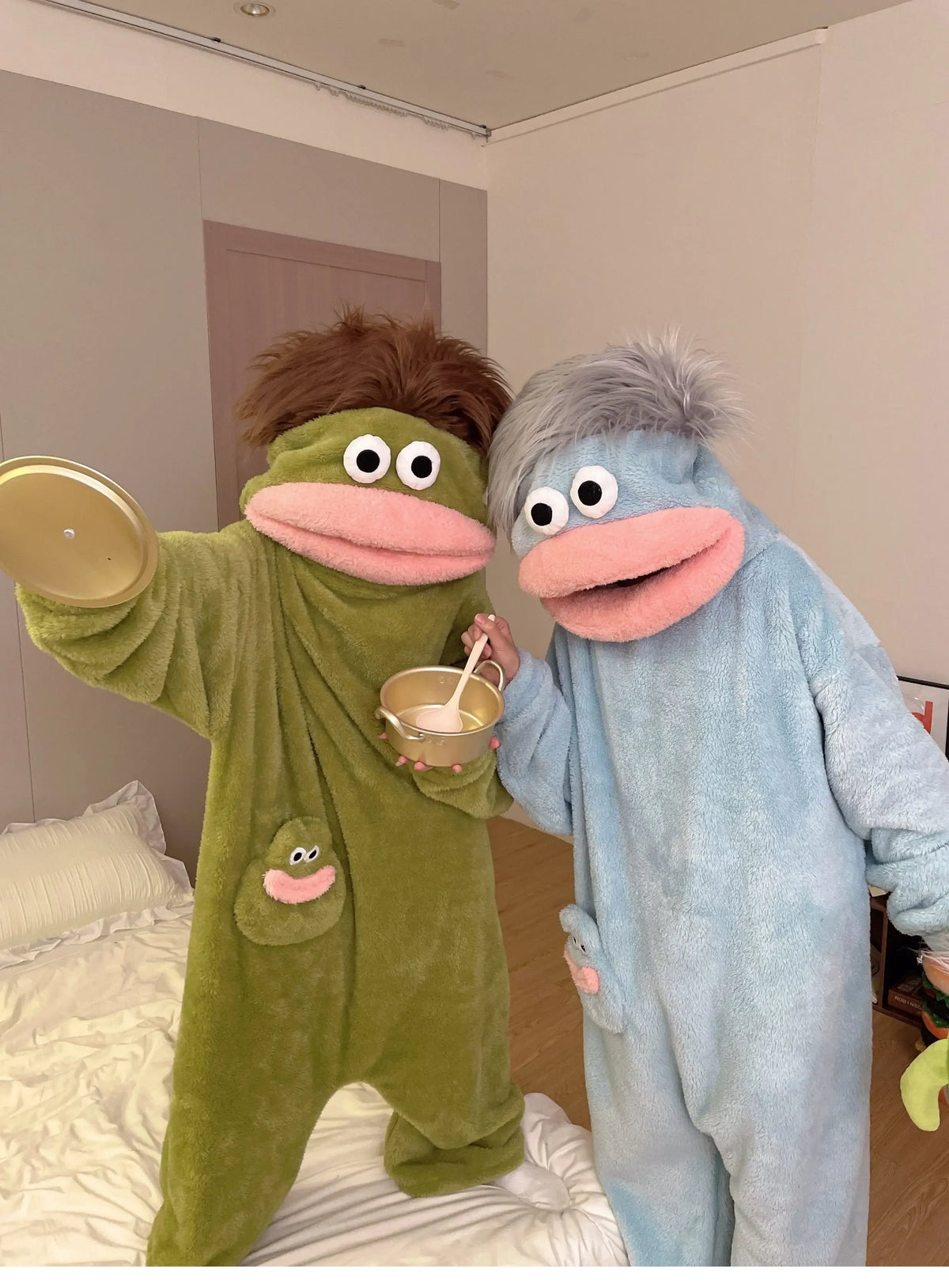 Two people in fuzzy monster onesies pajamas, one green and one blue, posing together.
