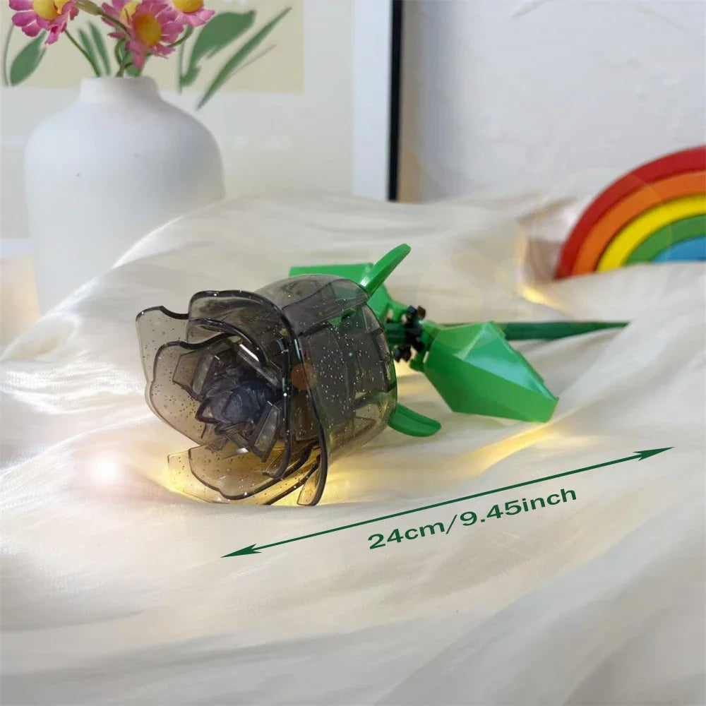 A clear glass rose flower building block bouquet with green stems and LED lights resting on a white fabric.