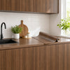A roll of self-adhesive wood grain wallpaper displayed on a kitchen countertop with white subway tile backsplash.