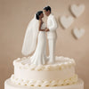 A white cake topper featuring a bride and groom figurine with a veil, set against a light background.