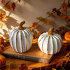 Elegant white and gold resin decorative pumpkins resting on a wooden surface with autumn leaves in the background.