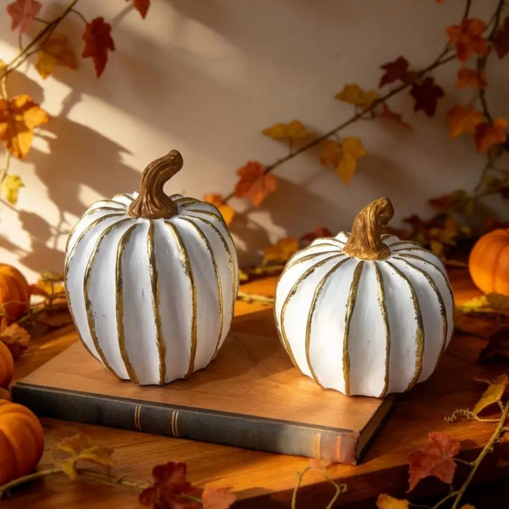 Elegant white and gold resin decorative pumpkins resting on a wooden surface with autumn leaves in the background.