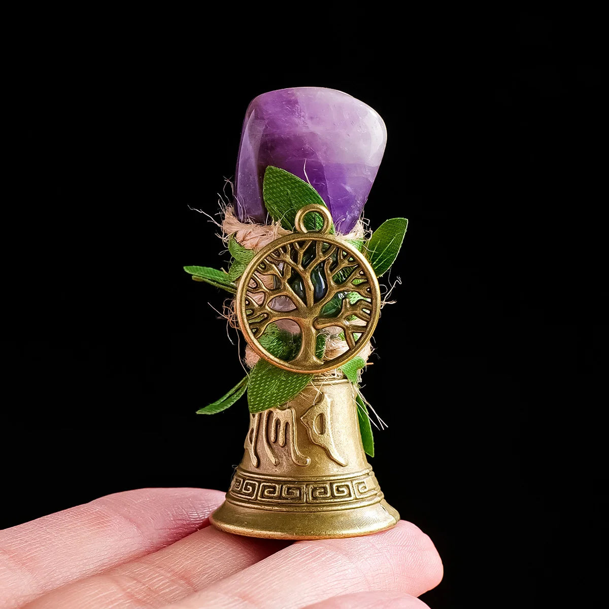 A purple crystal tree of life chime with a golden bell and green leaves held in a hand.