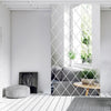 A modern interior featuring a gray sofa and a diamond-patterned mirror partition with natural light.