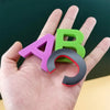 A hand holds a magnetic alphabet and number learning set showing the letters A and B in purple, green, and black.