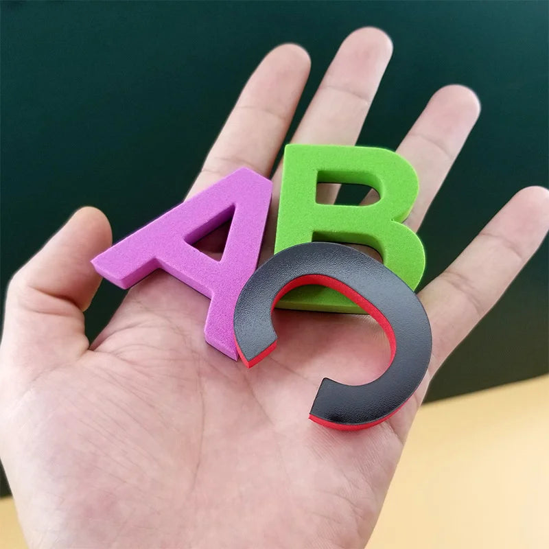 A hand holds a magnetic alphabet and number learning set showing the letters A and B in purple, green, and black.